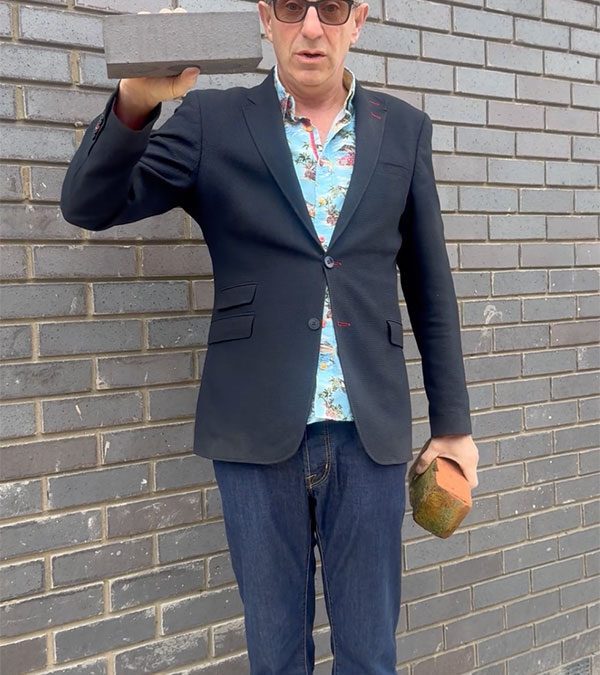 man holding bricks next to a grey brick wall